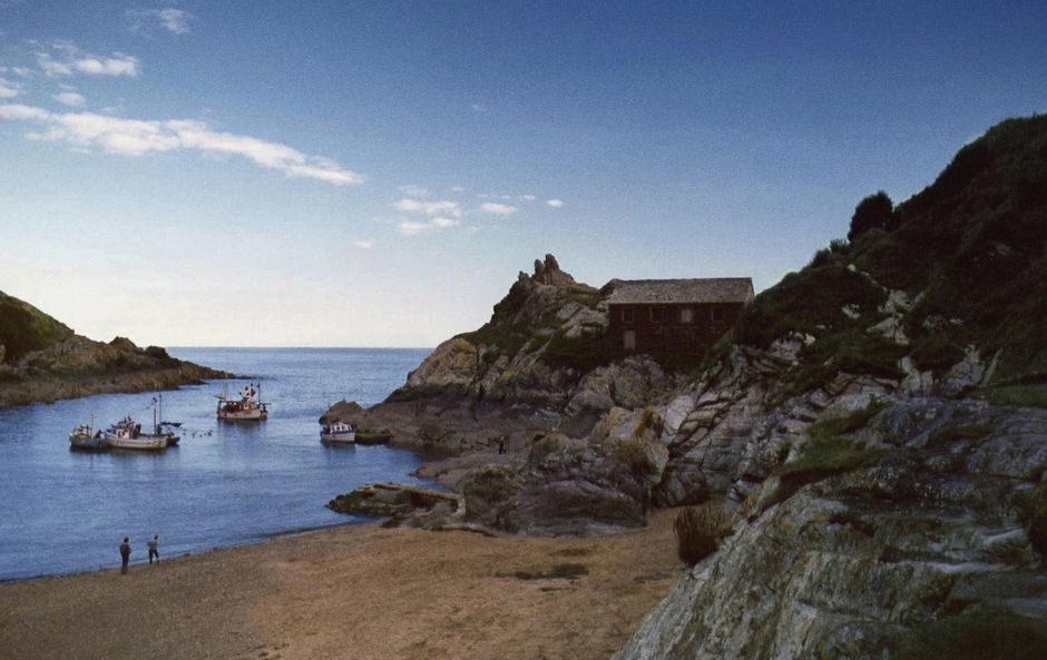 Idyllic view of Polperro harbor with fishing boats and coastal landscape, Cornwall, UK.